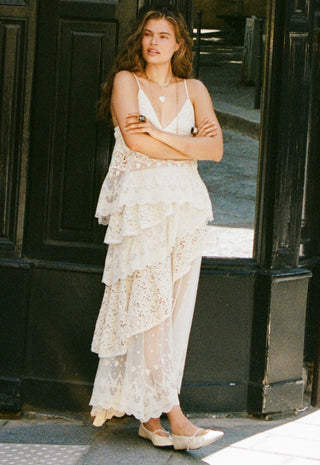  holding a small beige handbag and wearing white pointed flats.